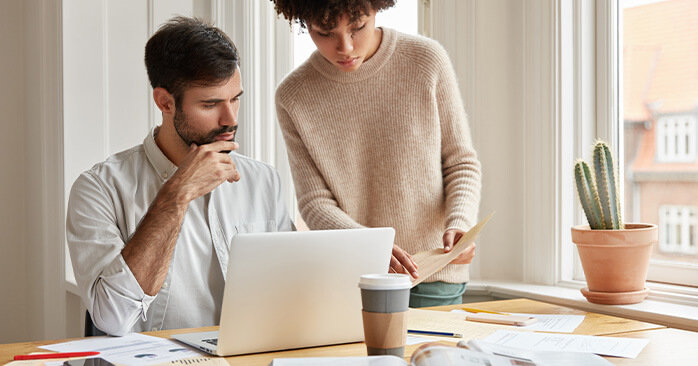 Couple doing research on computer while sitting by window.